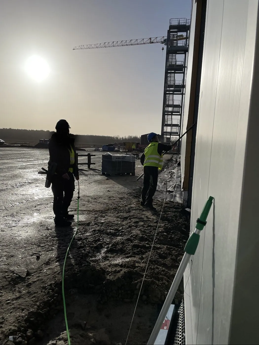 Zwei Mitarbeitende von feinsauber reinigen im Winter eine Fassade auf einer Großbaustelle